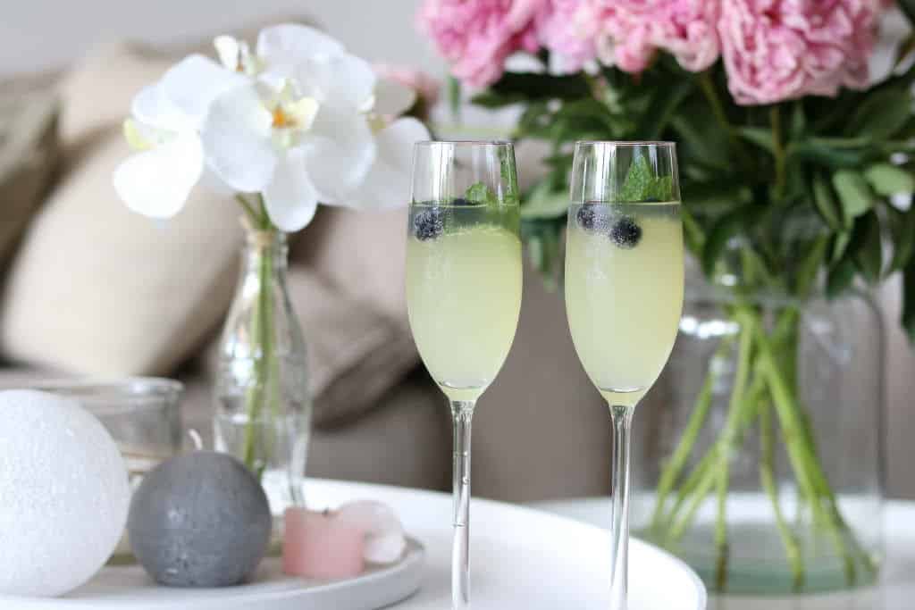 Een limoncello cocktail met home made limoncello, spa rood lemon, prosecco en een takje munt en blauwe bessen voor de decoratie.