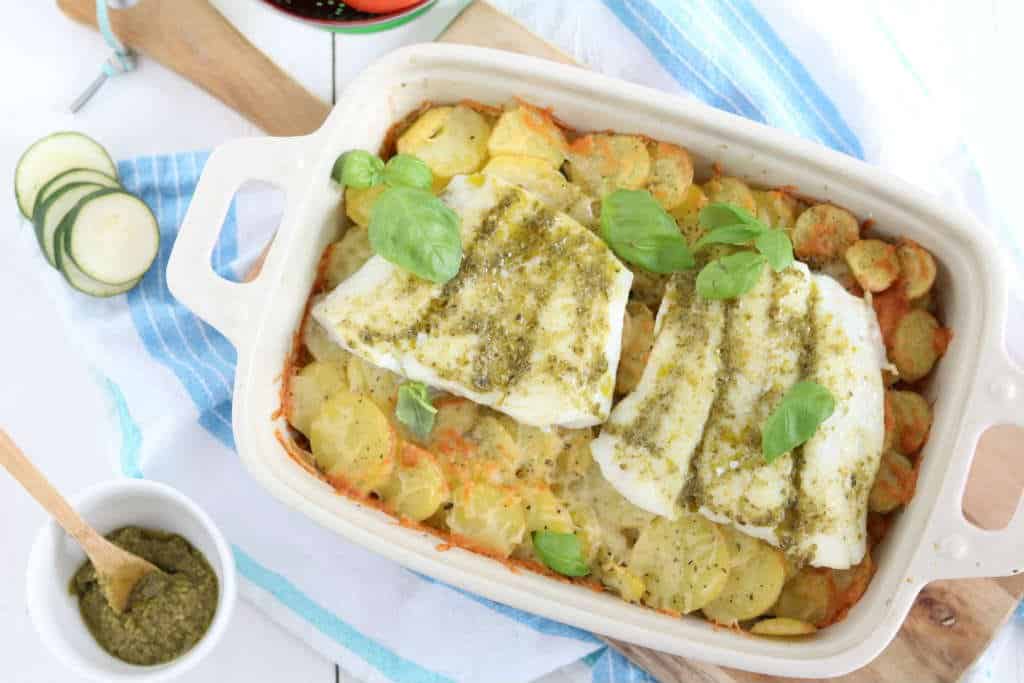 Ovenschotel met kabeljauw, courgette, tomaat en aardppelschijfjes. De vis wordt ingesmeerd met pesto.