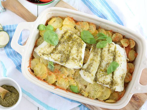 Ovenschotel met kabeljauw, courgette, tomaat en aardppelschijfjes. De vis wordt ingesmeerd met pesto.
